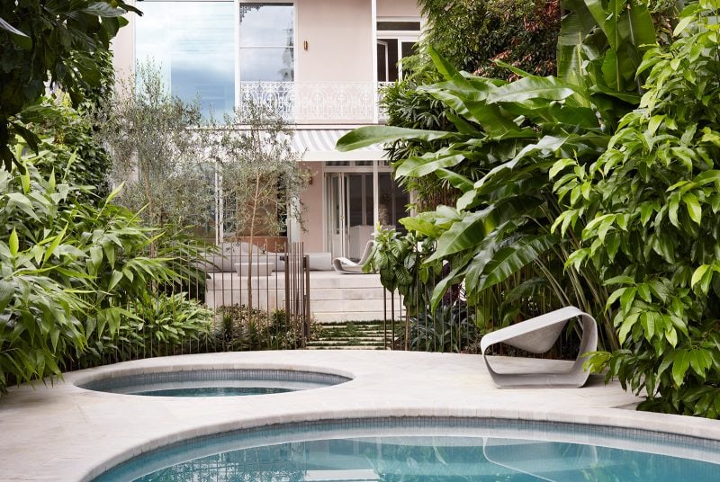 A view across the pool past lush tropical vegetation towards the Paddo Pool terrace, with its pink walls, white downpipes and filigree along its balcony