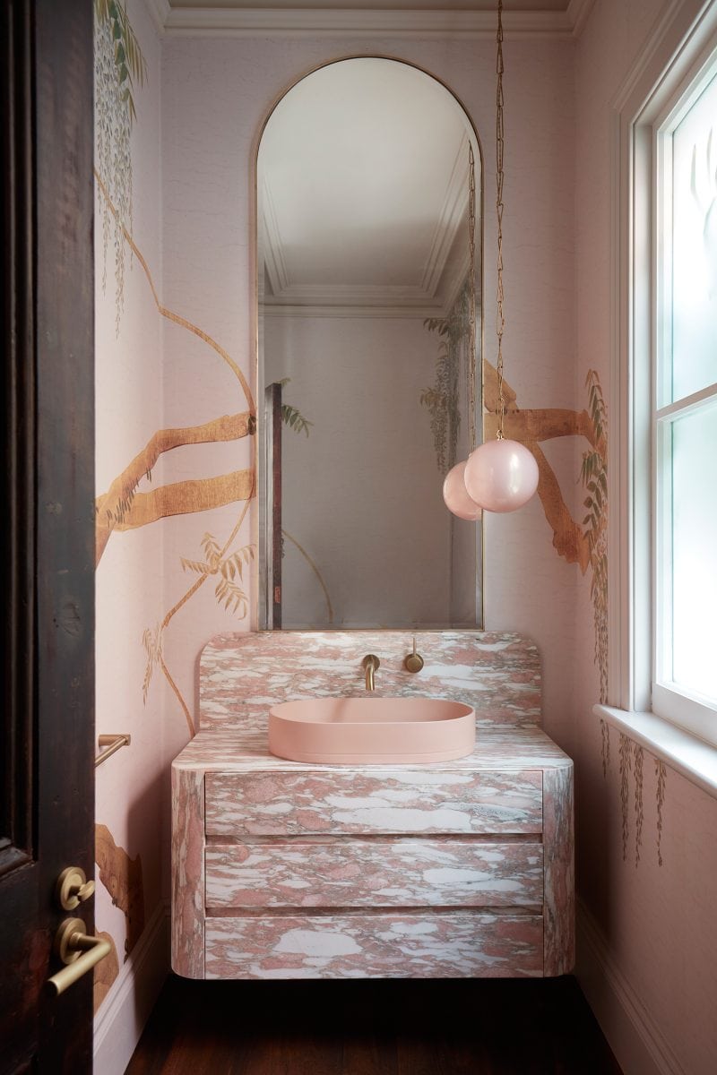 The powder room is thematically pink, with Calacatta Viola vanity, champagne patterned wallpaper, and pink pendant light and circle basin