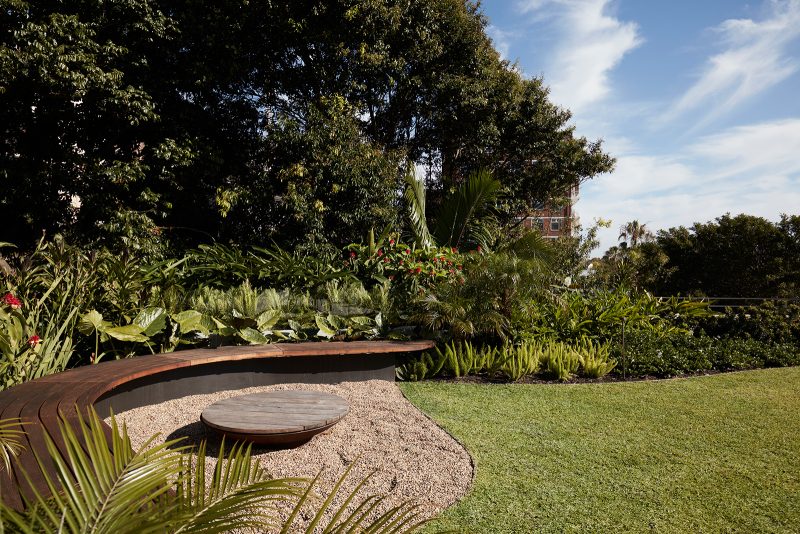 Timber curved benches around a stone fireplace, set in a manicured garden