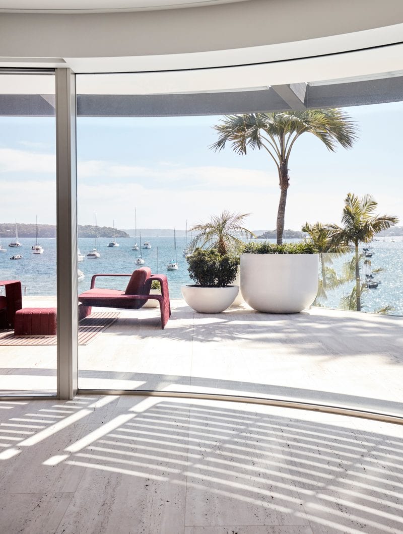 Luigi Rosselli outdoor sofa in red with potted palm trees next to it, overlooking sailboats in the Sydney harbour, apartment terrace