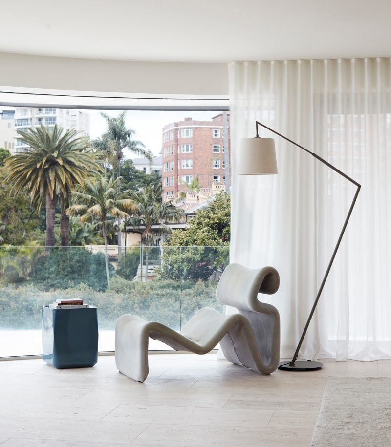 Luigi Rosselli, a comfortable sinuous grey armchair enjoys the sunlight from the full-height window, with a panoramic view of the lush greenery outside