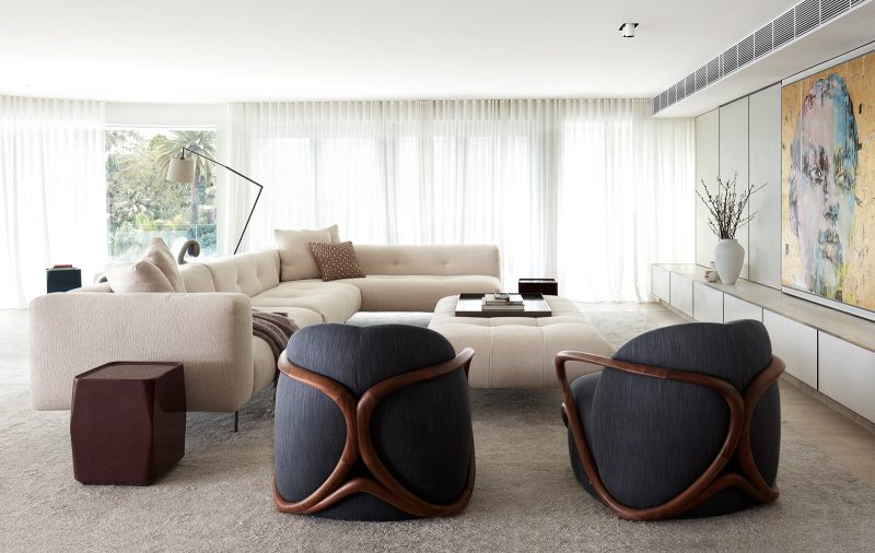 Luigi Rosselli, a restrained living room design with creamy palate, punctuated by dark blue arm chairs and a statement gold wall art of a woman's face