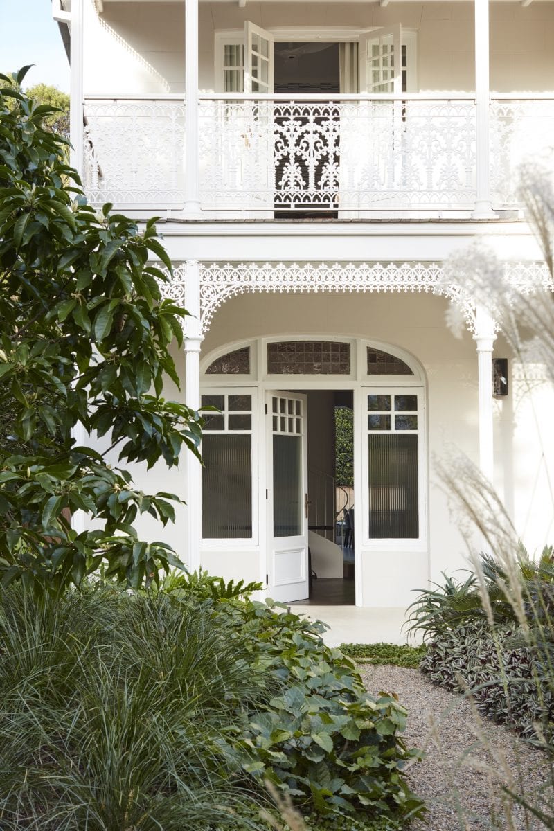 Beneath a filligree adorned porch, the front door, which consists of fluted glass panels set in a timber white frame, opens into the hallway