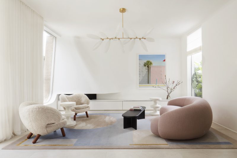 Opposite the dining area, the living room painted in a creamy palate and blond timber flooring, with pink voluptuous sofa and woolly white armchairs