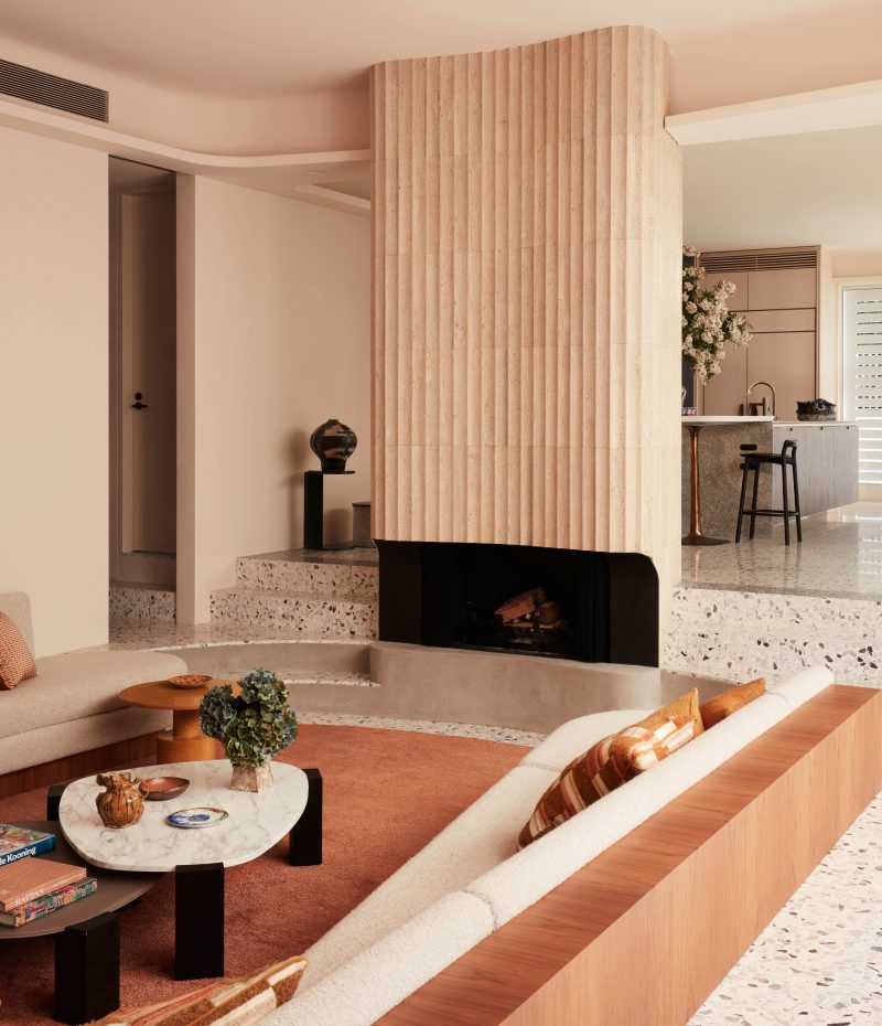 autumn palette, terrazzo steps leads from the dining room down into the sunken lounge with an orange rug, cream fluted tiles transform the fireplace into the centerpiece