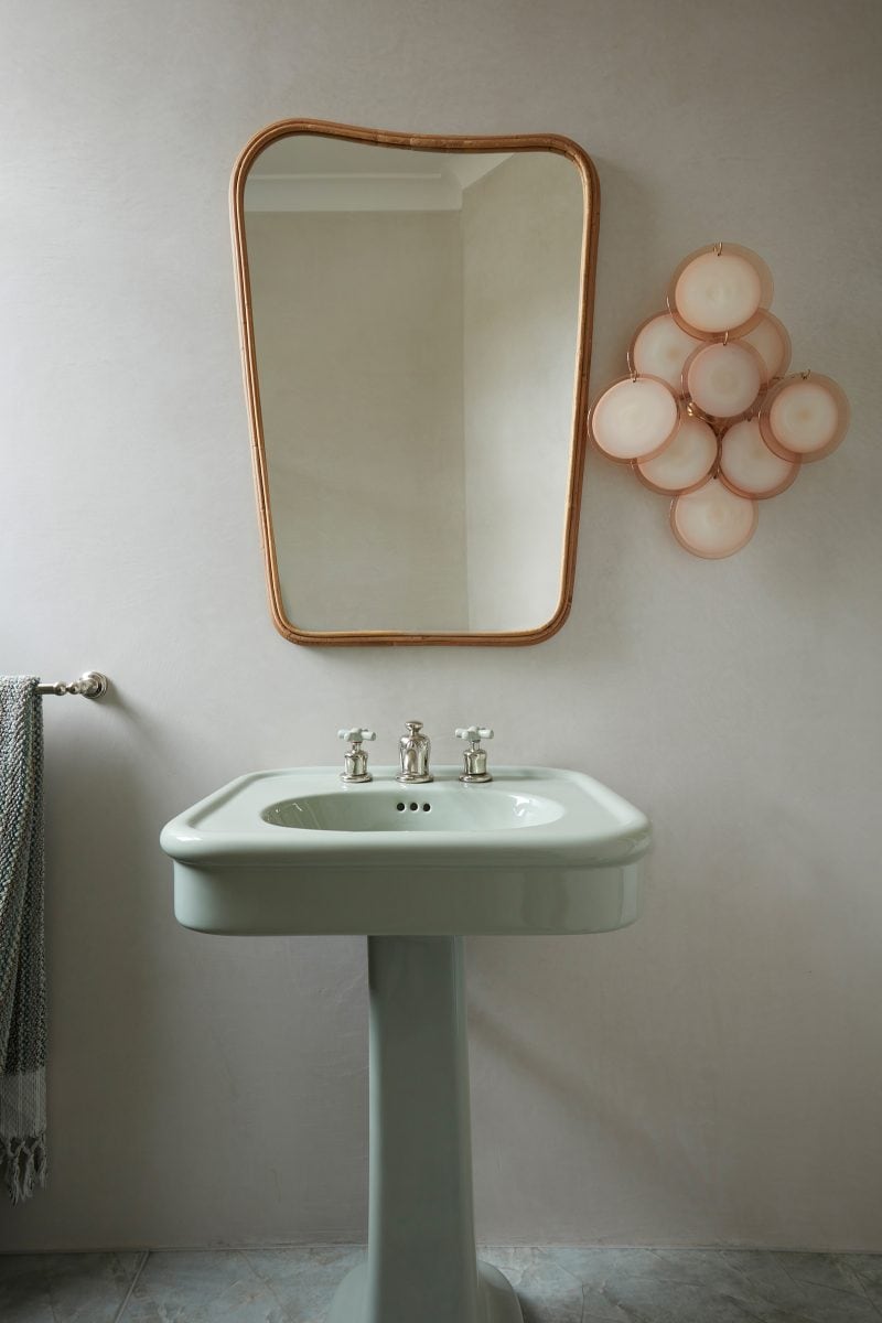 traditional ceramic sink in soft mint green with silver taps, irregular-shaped mirror framed in timber, vintage Murano wall disc scones